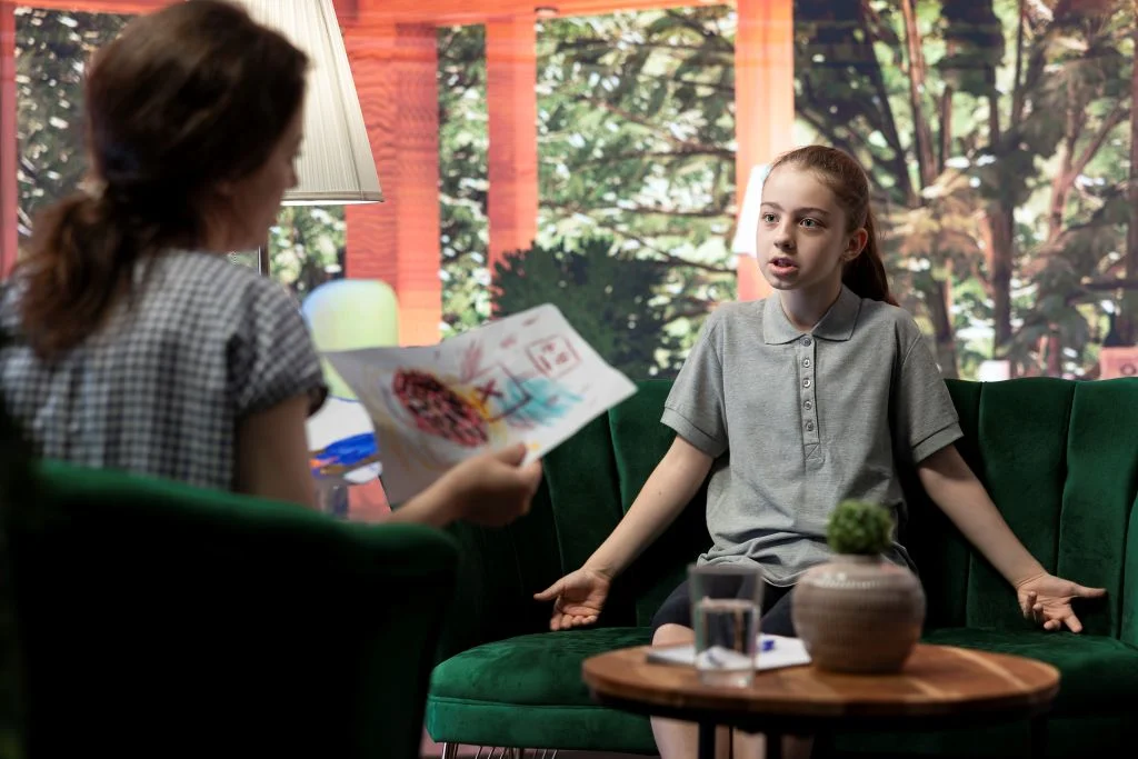 Psikolog ile duygularını paylaşan çocuk, özgüven geliştirme sürecinde imge terapinin uygulandığı bir terapi seansında.